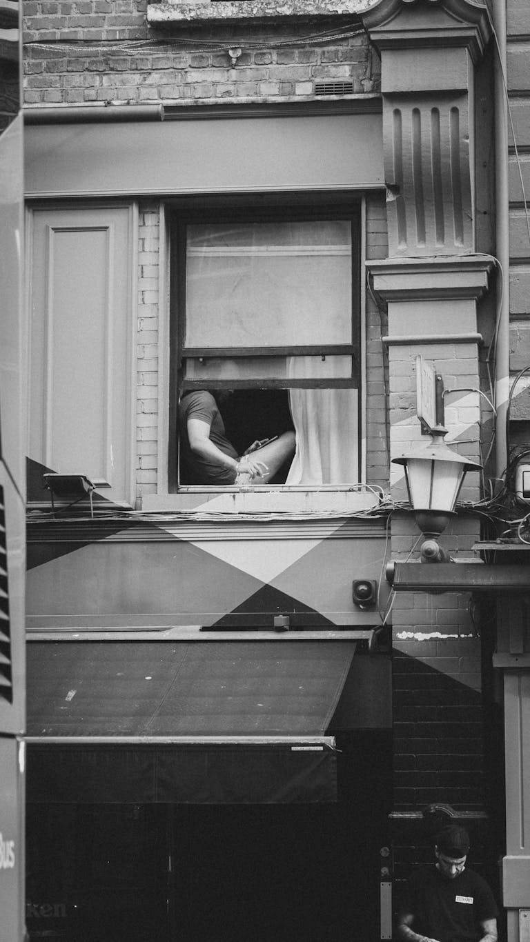 A moody black and white photo of an urban building with a person at the window.