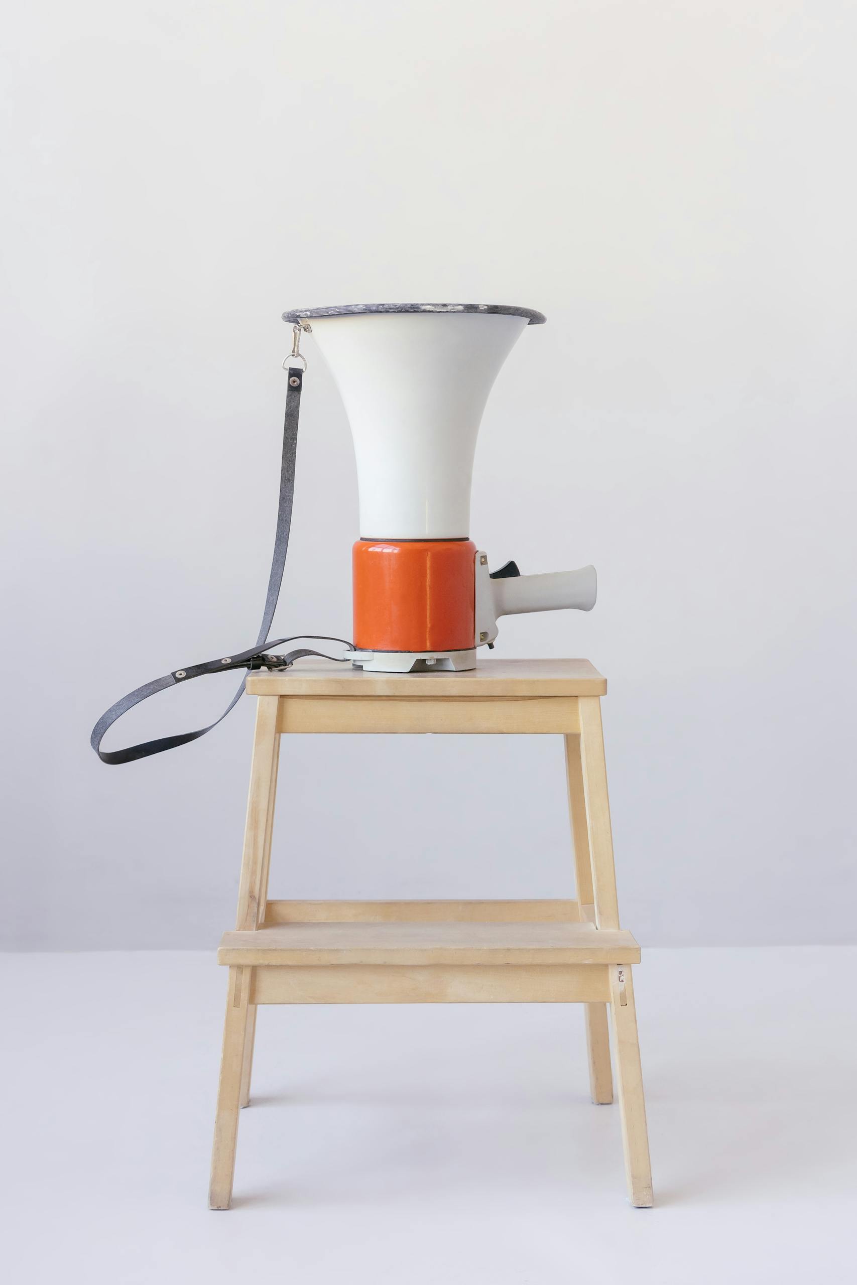 A red and white megaphone placed on a wooden stool against a minimalist background.