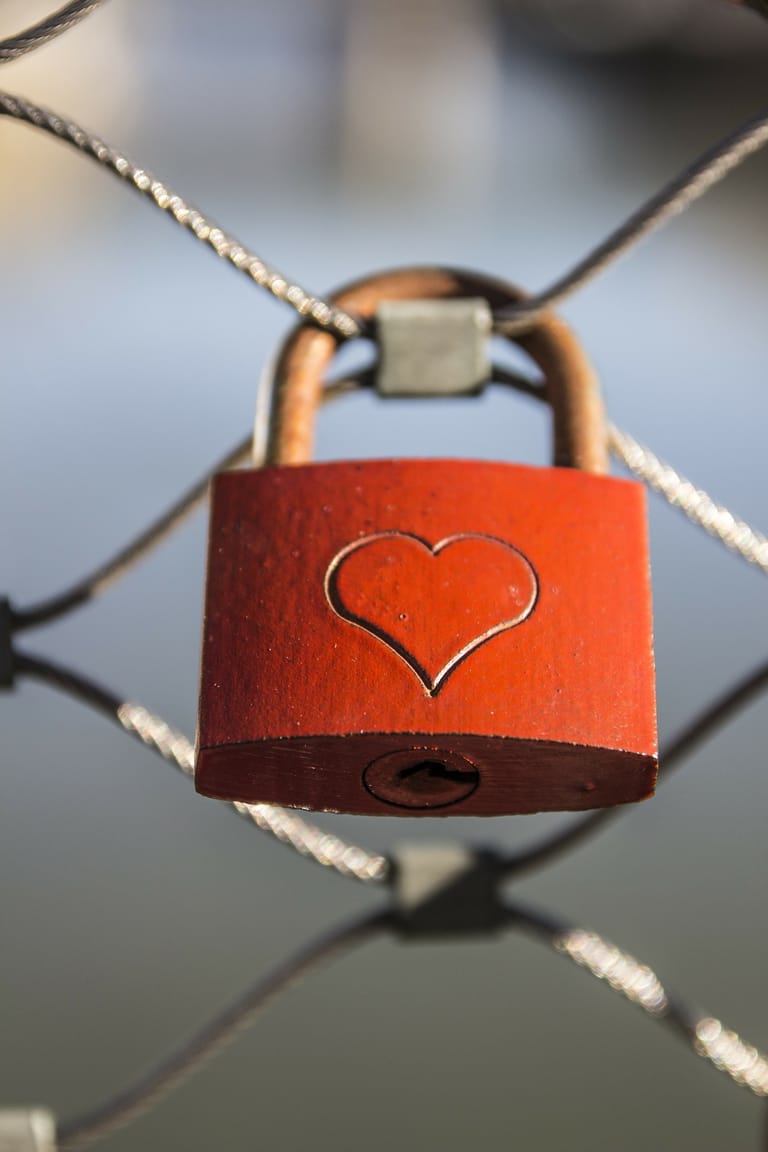 A red love padlock with a heart engraving attached to a wire fence.