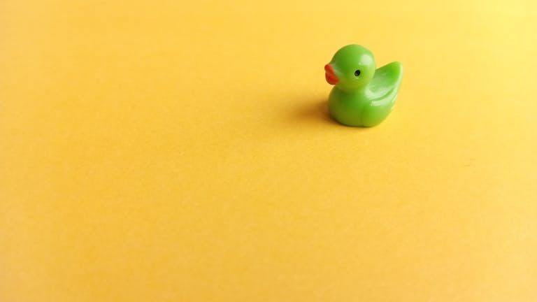 A small green toy duck isolated on a vibrant yellow background for a playful mood.