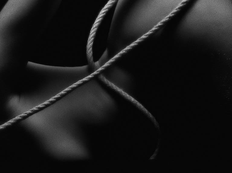 An artistic black and white nude photo with rope details, highlighting aesthetic contours.