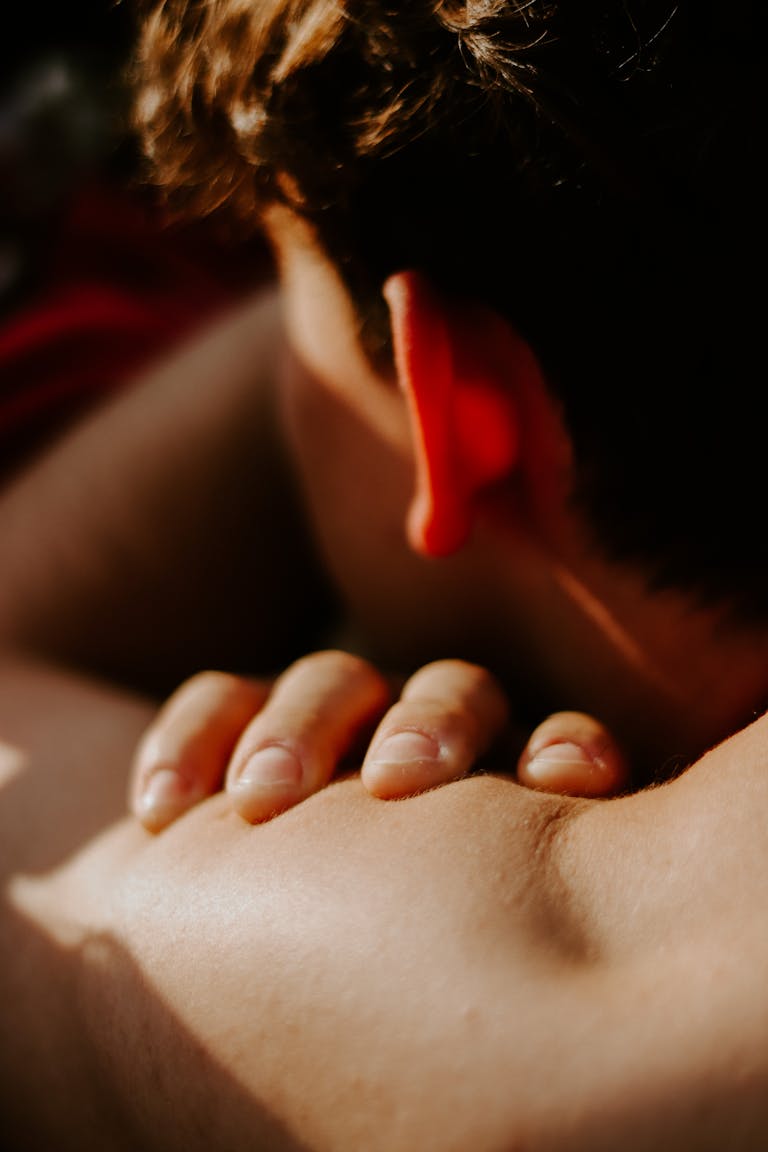 An intimate close-up of a man's hand gently resting on his shoulder in warm sunlight.