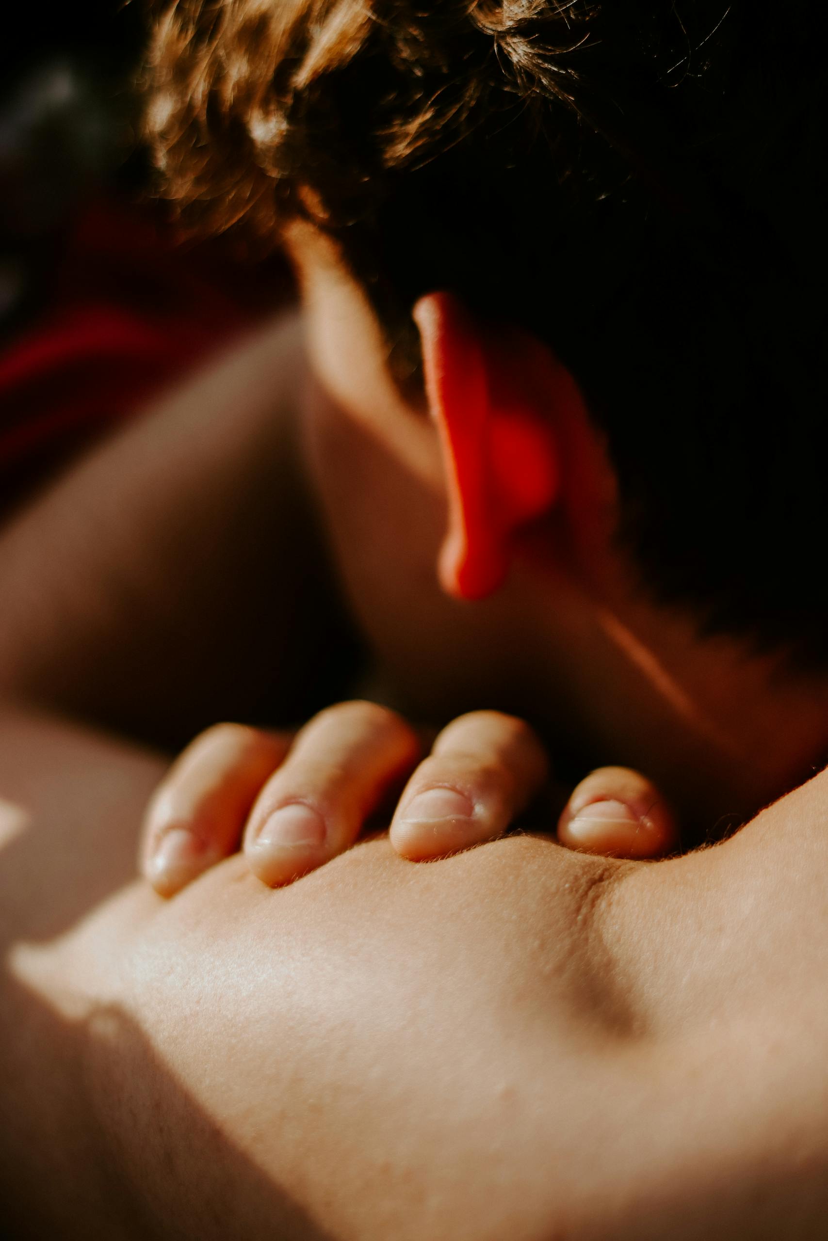 An intimate close-up of a man's hand gently resting on his shoulder in warm sunlight.