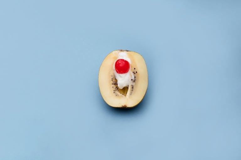 Artistic presentation of a kiwi with cream and cherry on a blue background.