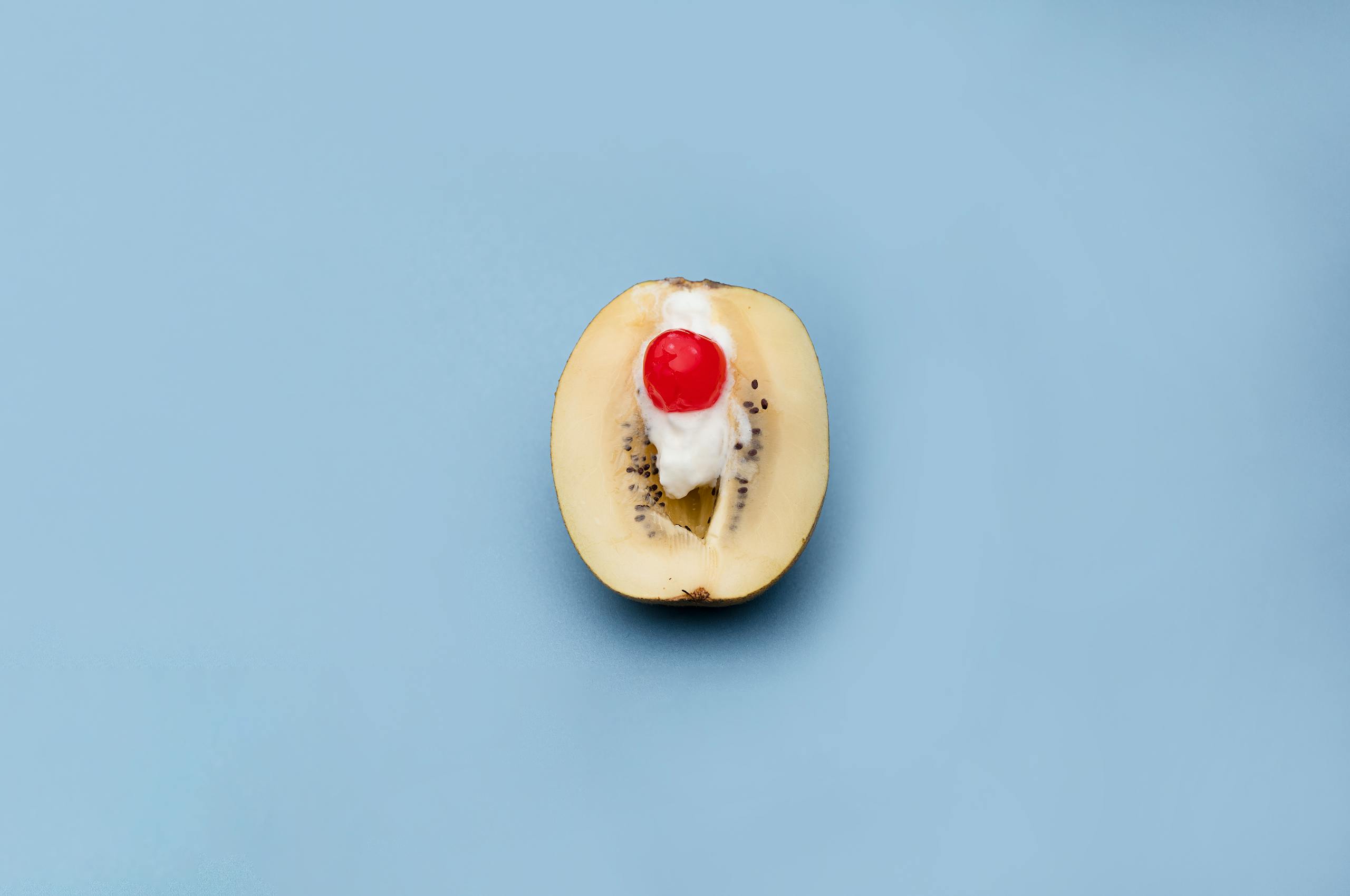 Artistic presentation of a kiwi with cream and cherry on a blue background.
