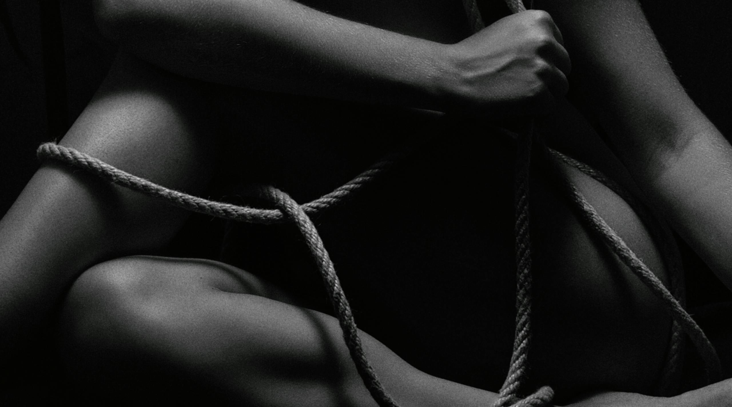 Black and white image of a person intricately tied with rope.
