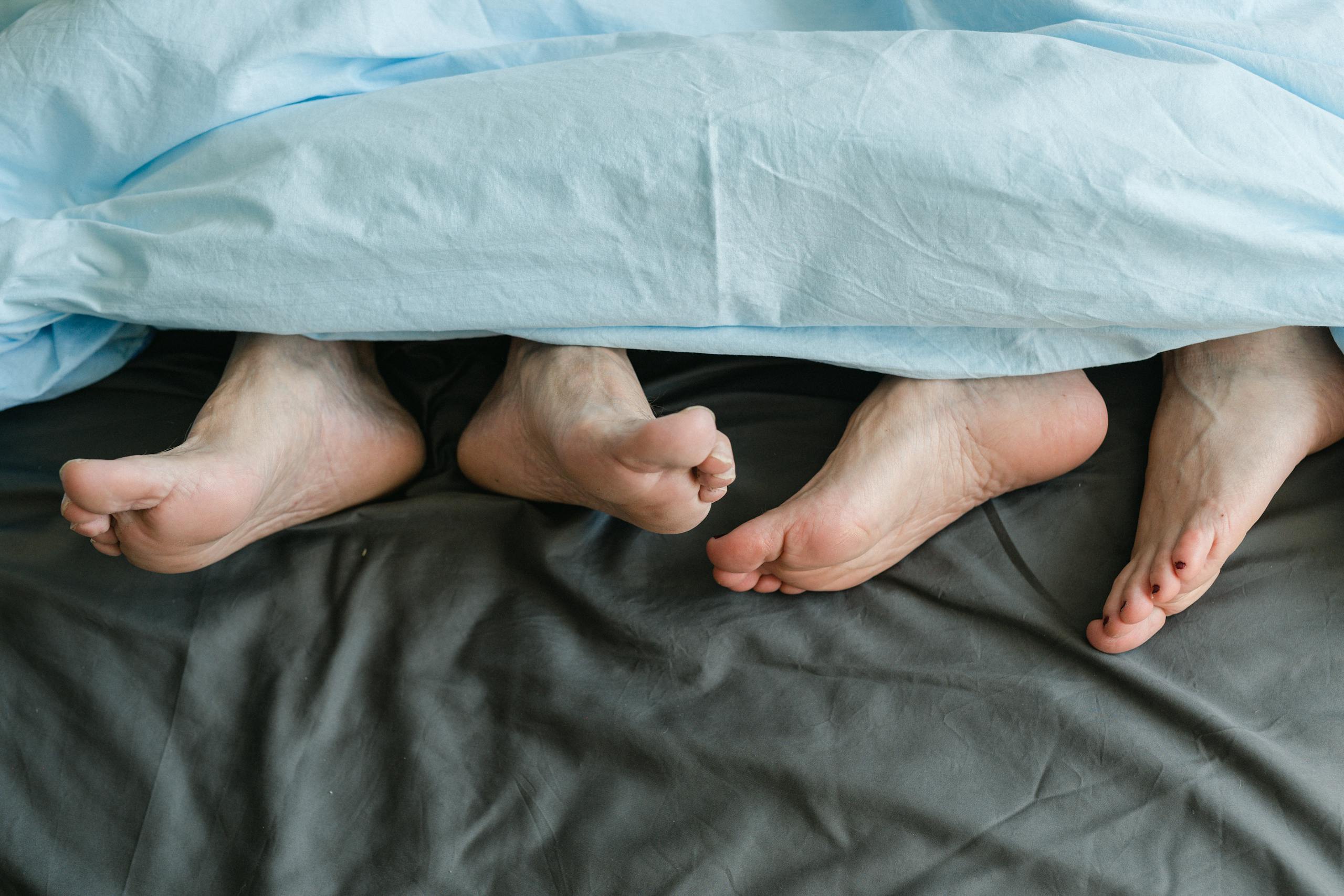 Close-up of feet peeking from under a blanket in a cozy setting.