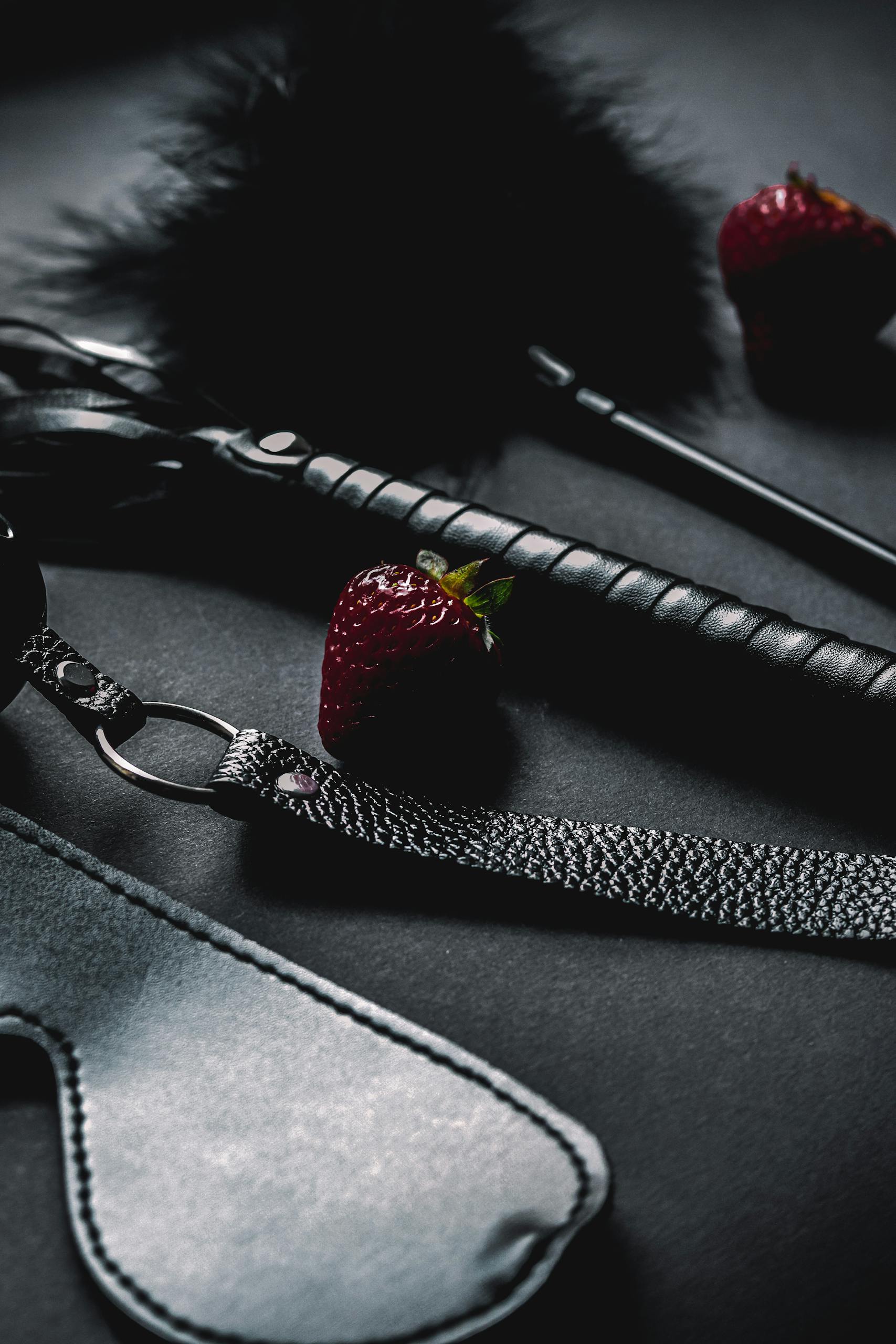Close-up of intimate accessories and strawberries on a dark surface, creating a moody vibe.