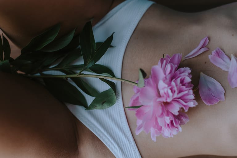 Close-up of pink peony petals on skin with a white garment, creating a sensual art piece.