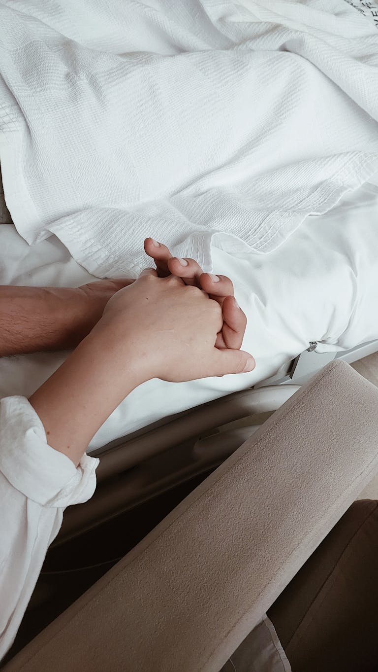 Close-up of two hands holding on a bed, symbolizing intimacy and support.