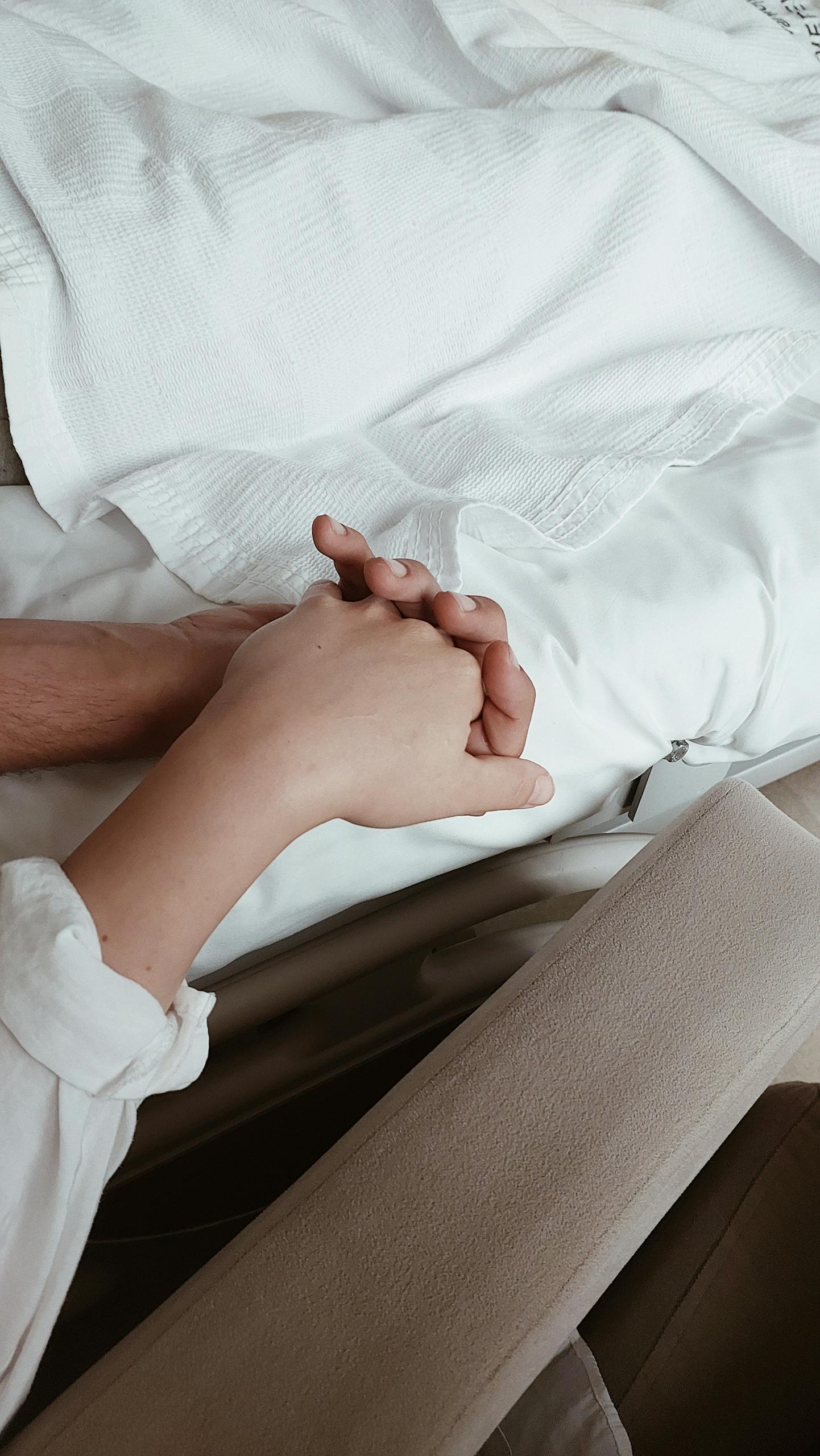 Close-up of two hands holding on a bed, symbolizing intimacy and support.