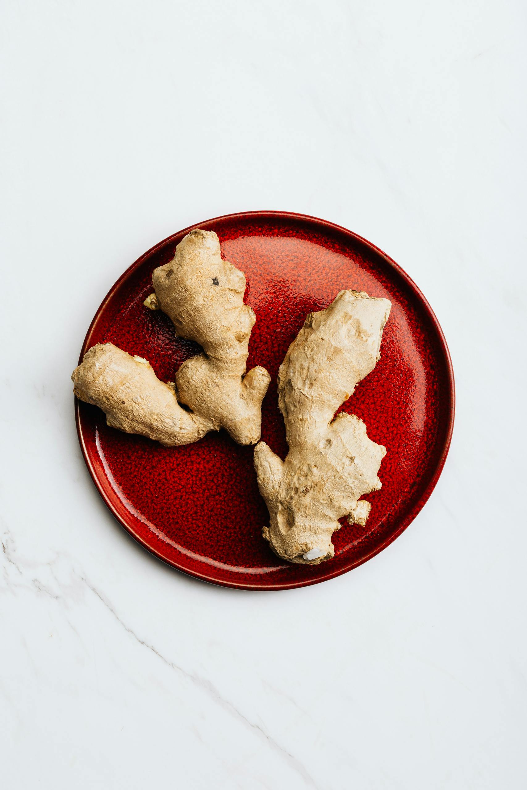 Fresh ginger root on a vibrant red plate, perfect for healthy culinary use.