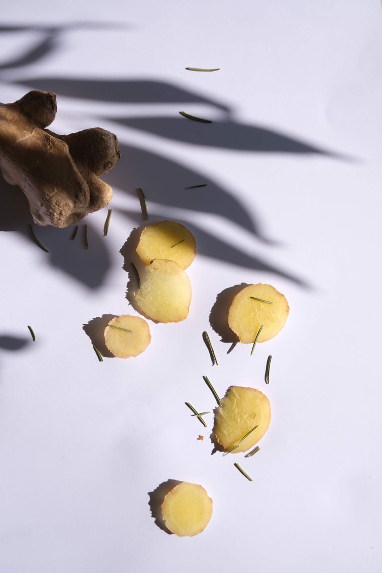 Ginger slices with rosemary on a white surface, creatively lit with shadows. Perfect for food and culinary themes.