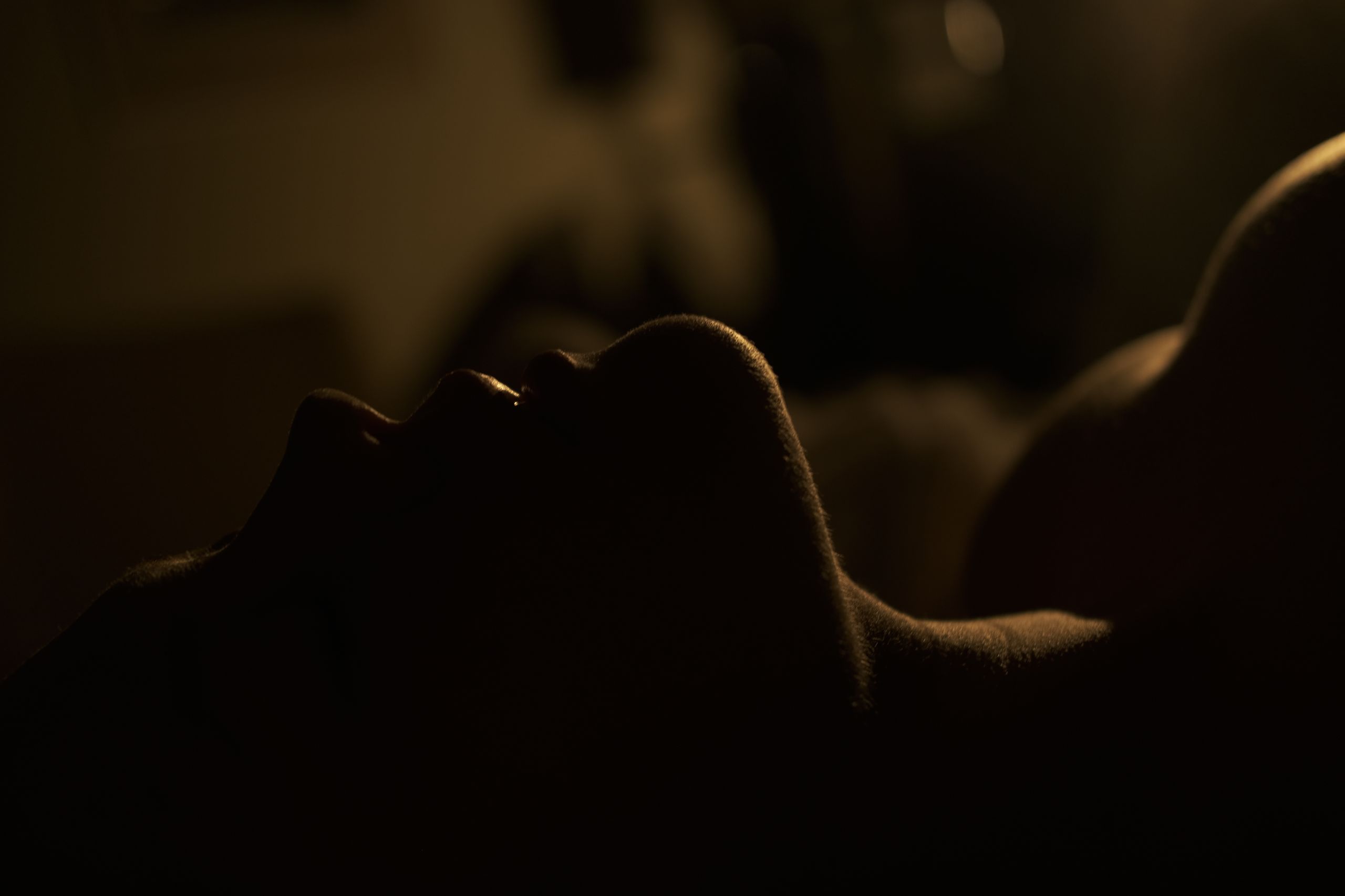 Young female with bare shoulders lying alone in dark room with closed eyes and sunlight on body