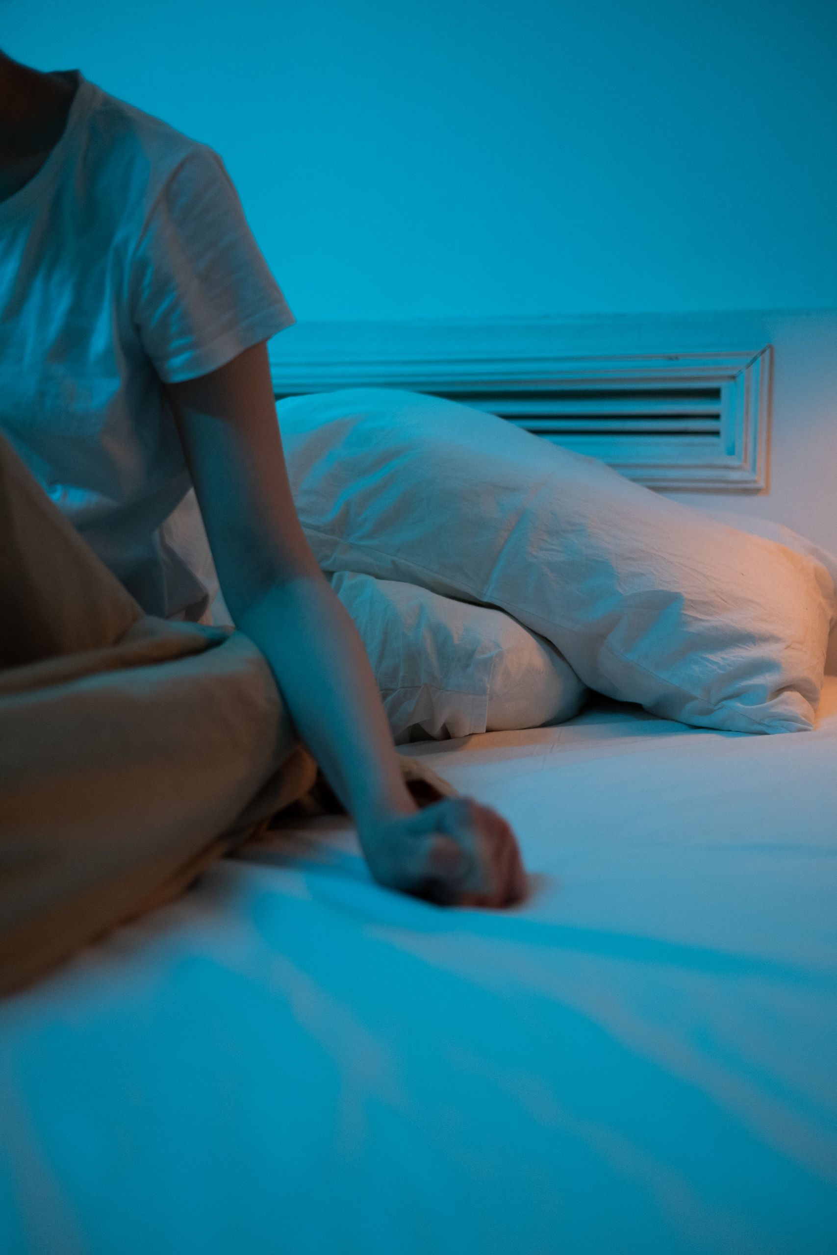 A person sitting on a bed in a dimly lit room, conveying a moody atmosphere.