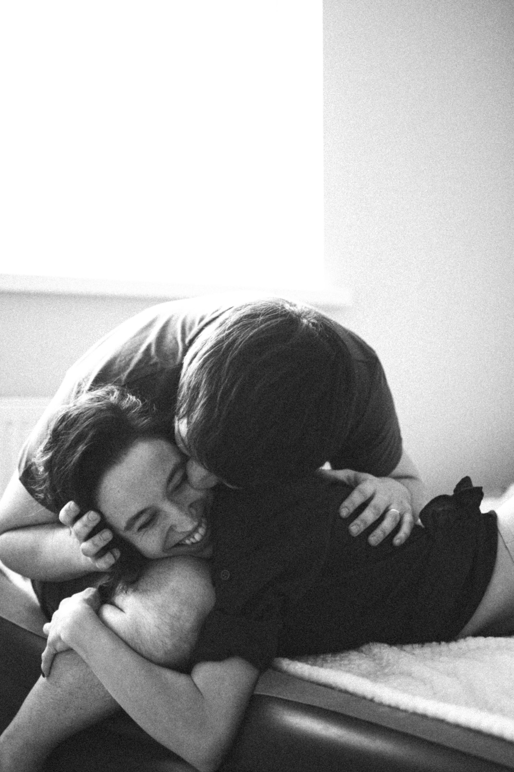 Black and white photo of a couple embracing playfully indoors, showcasing joy and affection.