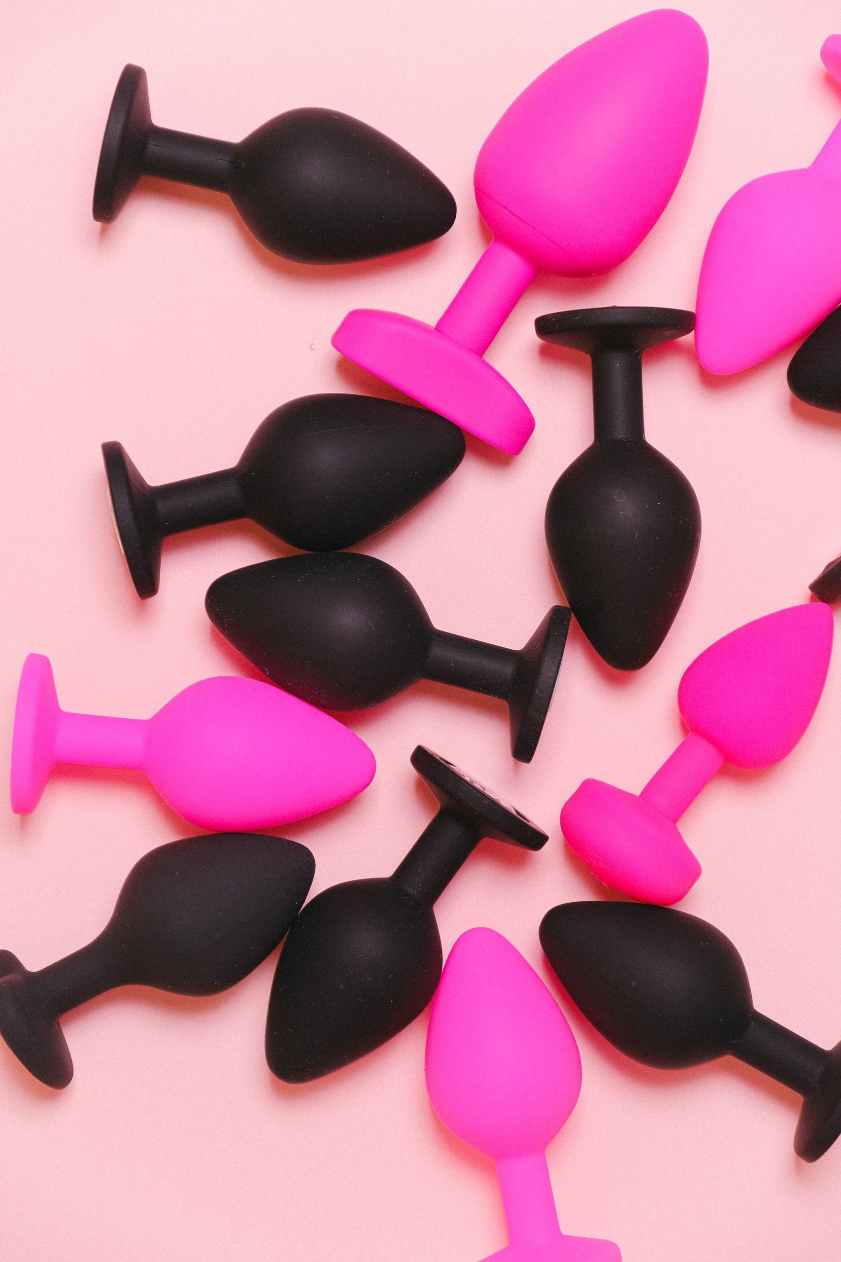Colorful silicone butt plugs arranged on a pink background for adult toys display.