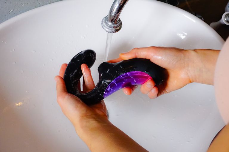 Hands cleaning a waterproof vibrator under running water in a sink.
