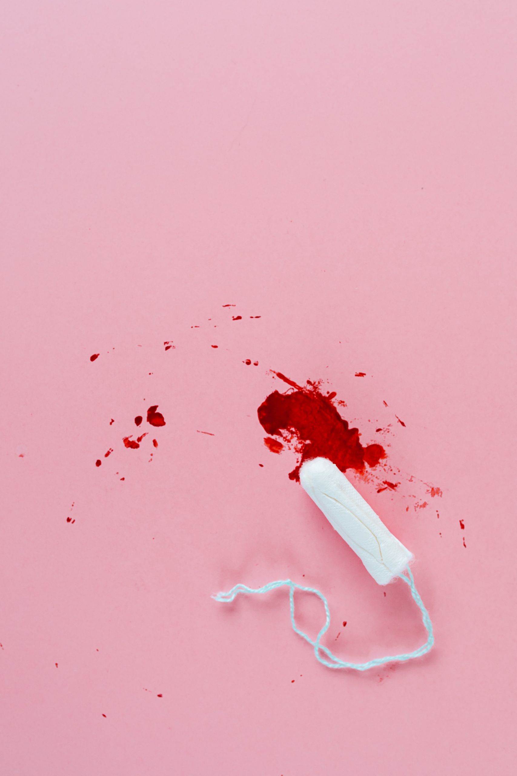 Tampon on pink background with blood stains, emphasizing menstrual hygiene.